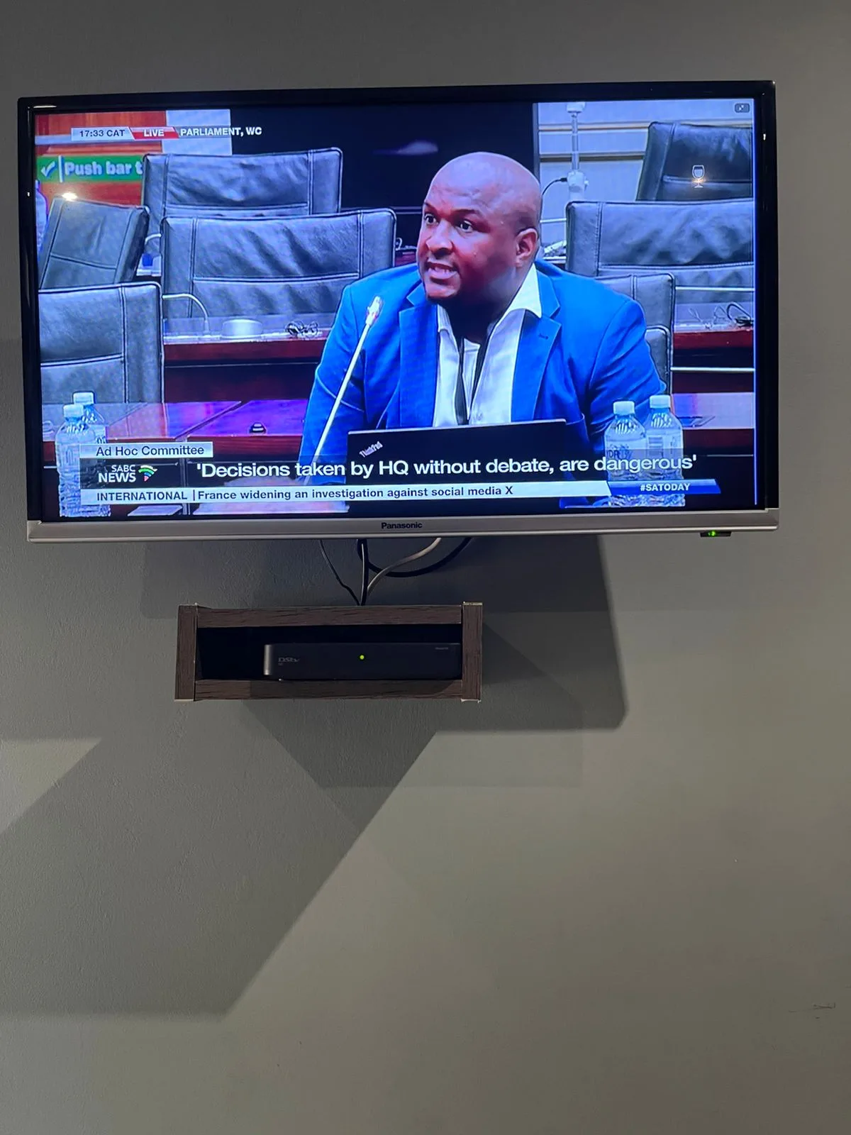 Wall-mounted TV with recessed DSTV decoder cubby tuned to SABC news