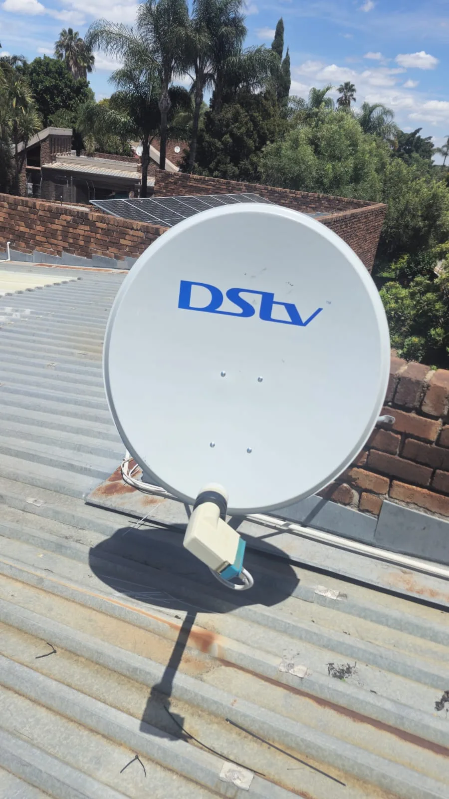 DSTV satellite dish installed on a metal roof beside solar panels
