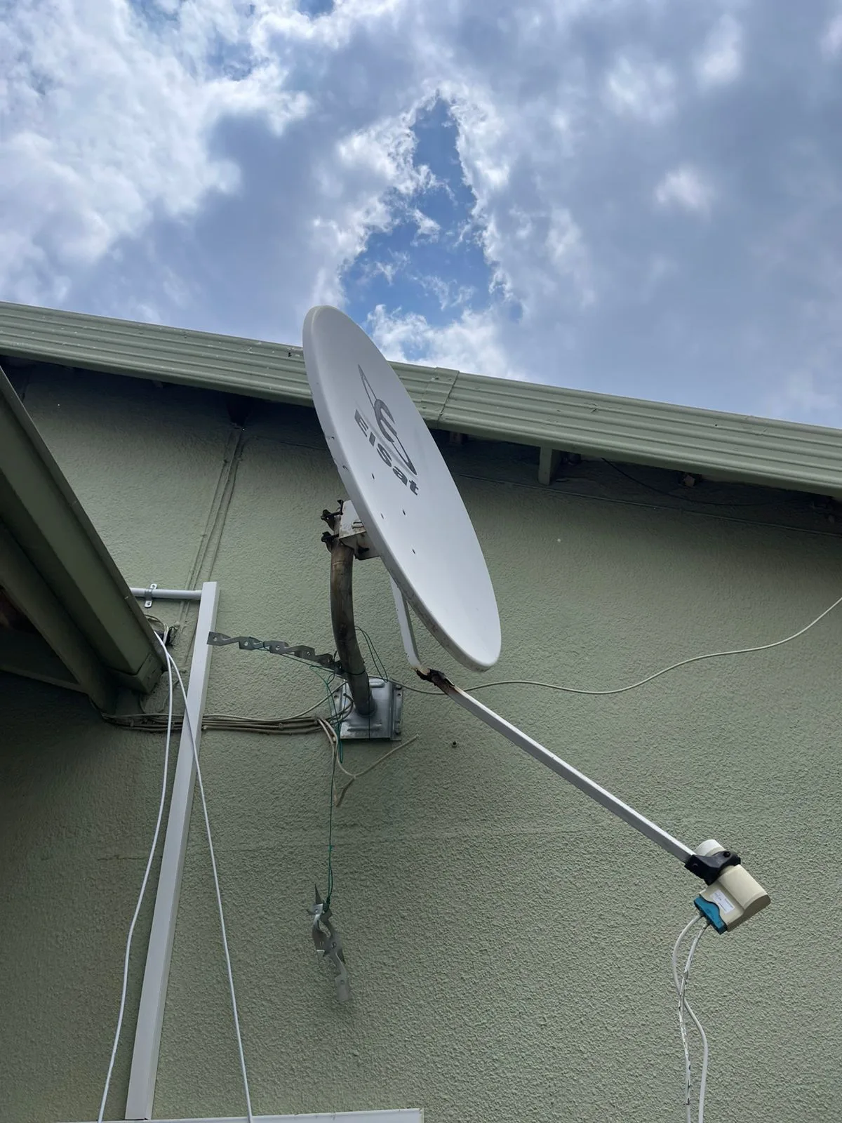 Close-up of an Elsat satellite dish fixed to a green stucco exterior wall