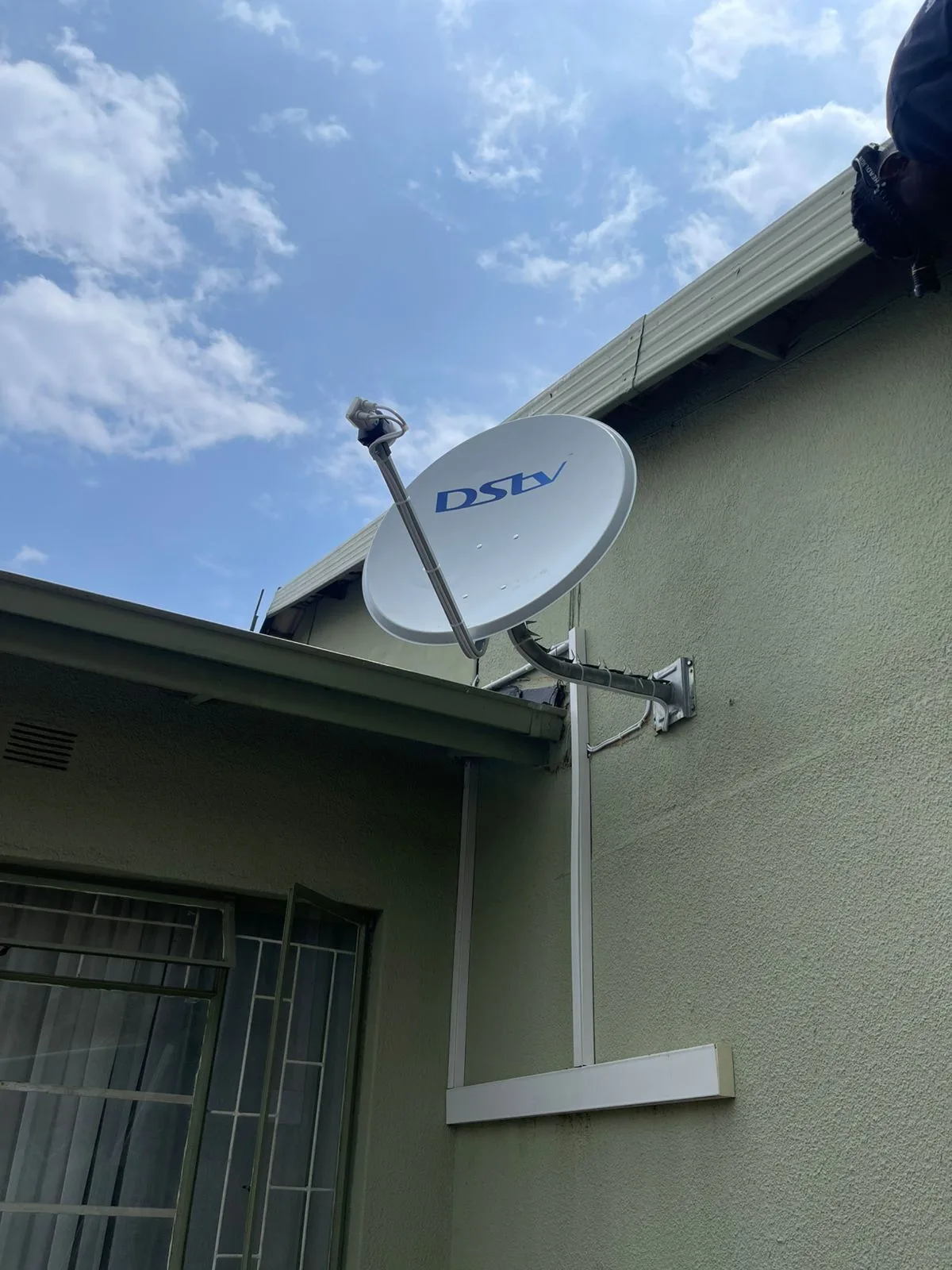 DSTV satellite dish wall-mounted on a green stucco suburban home